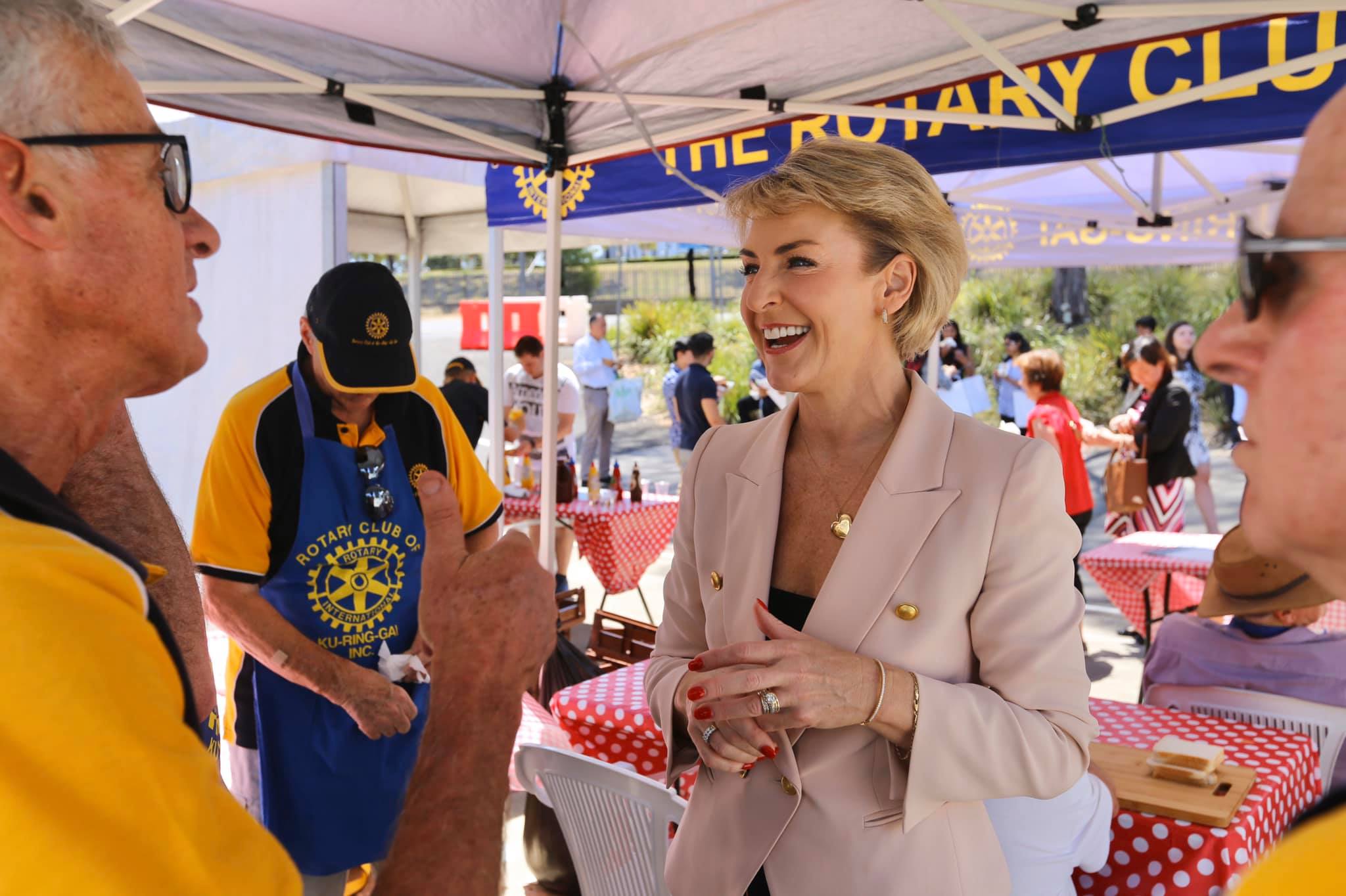 Michaelia Cash laughing while speaking with Rotary volunteers at an outdoor community stall.
