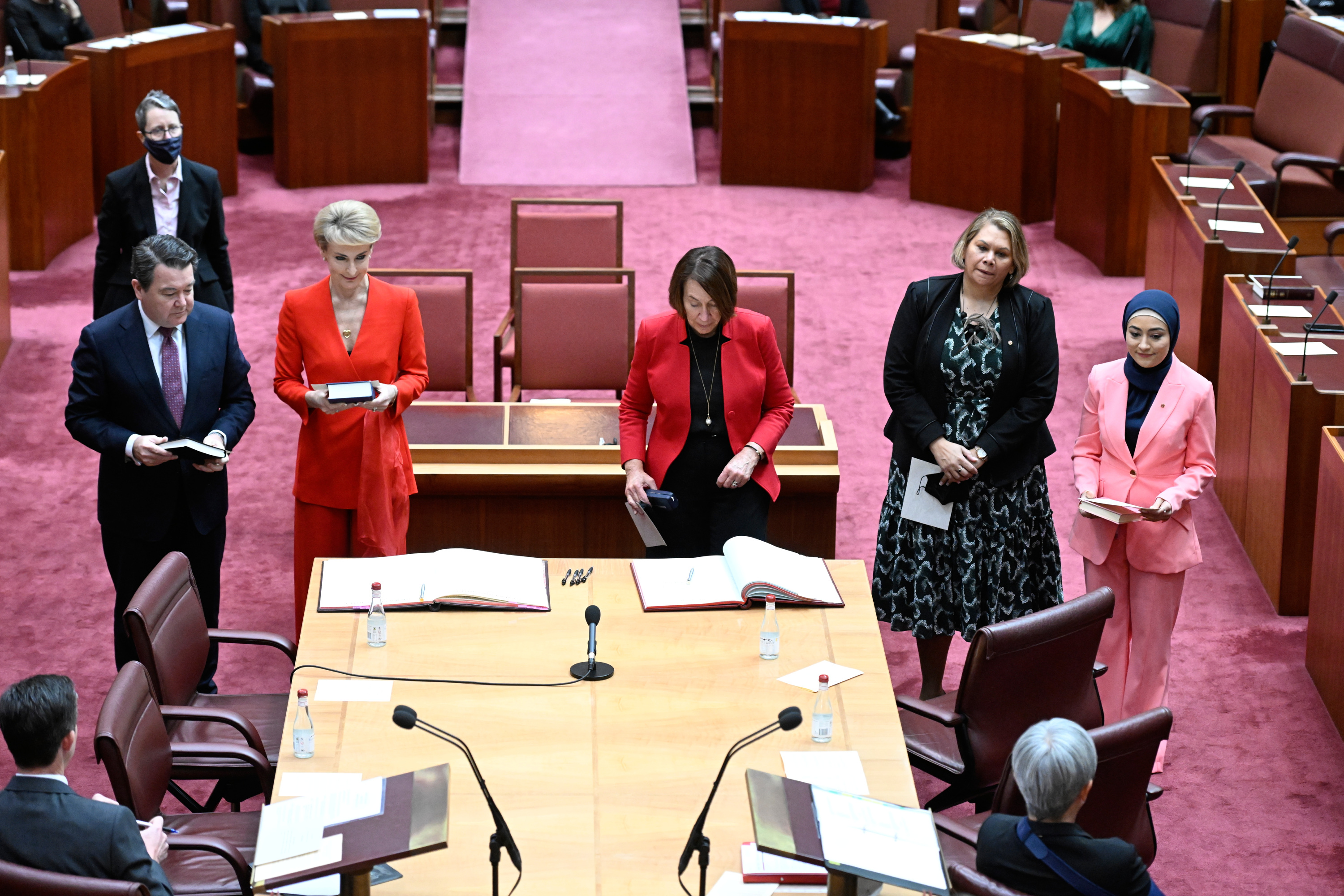 Michaelia Cash, in a red suit, standing with four colleagues in the Australian Senate chamber.